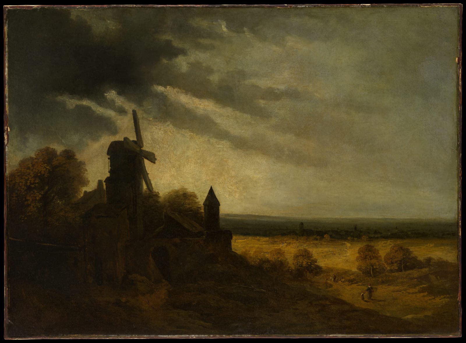 A windmill on a dark rise, its sails motionless under a heavy sky, with a lit empty plain stretching away behind it.